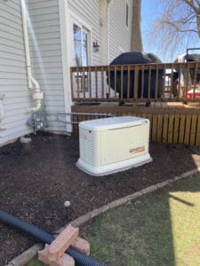A Generac generator is installed outside a house next to a wooden deck.