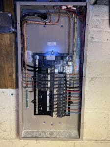 Electrical panel with organized wiring and labeled circuit breakers mounted on a wall.