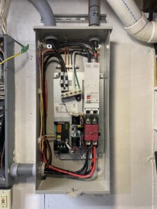 An open electrical panel showing various wires, circuit boards, and components mounted on a wall.