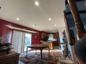 A dining area with a round table on a colorful rug. Large sliding doors let in natural light. The space connects to a kitchen with wooden cabinets and decor along the walls and staircase.