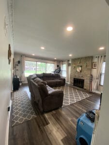 A living room with a sectional sofa, patterned rugs, a stone wall with a fireplace, and large windows displaying a garden view.