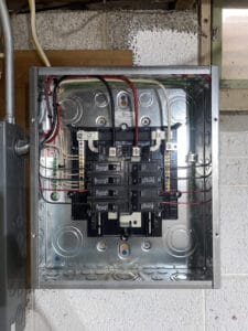 An open electrical panel with multiple circuit breakers and wiring inside a metal box, mounted on a wall.