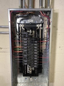 An open electrical panel with neatly arranged wires and circuit breakers mounted on a wall.