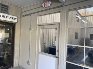 A door with a small window is adjacent to a food pantry sign. An exit sign is above the door, and a large exterior window is on the right.